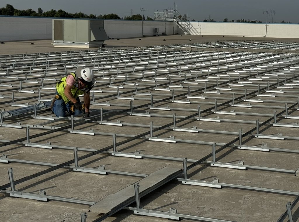 Safety professional in a hard hat and hi-vis vest installing racking on a commercial solar rooftop